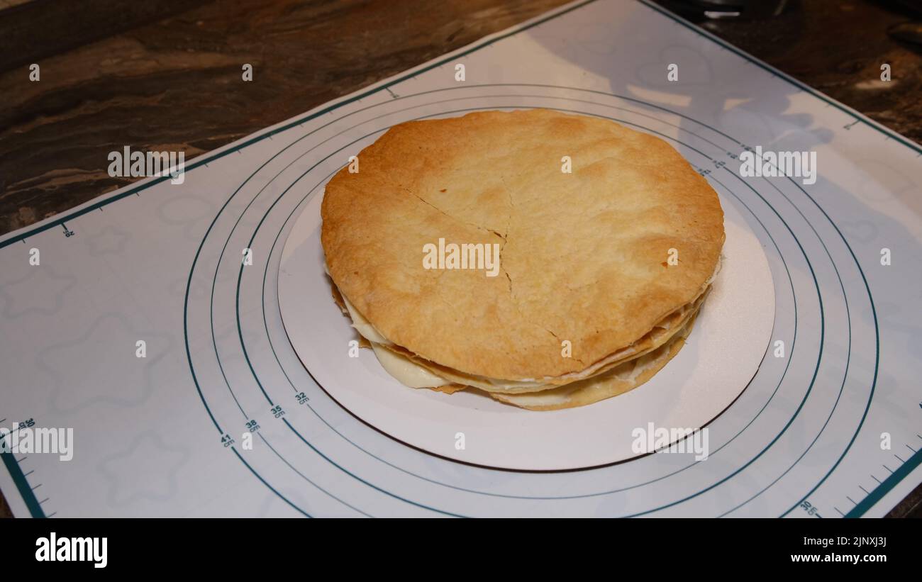 Die Hand des Mannes setzt die Creme auf den Kuchen, die Kuchendekor. Napoleonkuchen mit Creme machen. Stockfoto