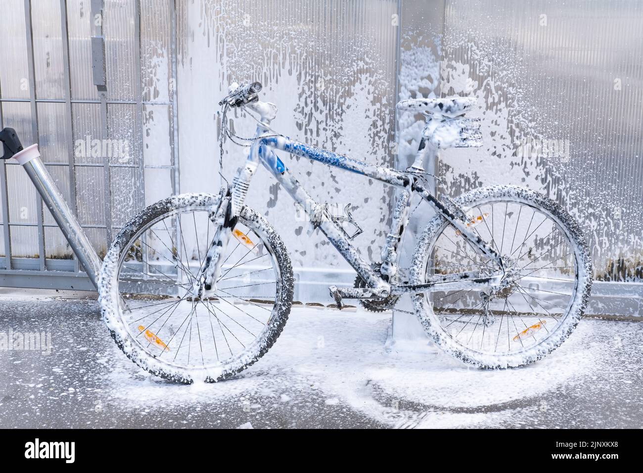 Waschen eines Fahrrads mit einem Schaumstrahl bei einer Autowäsche. Das Fahrrad ist mit Schaumstoff überzogen. Self-Service. Fahrradwartung. Stockfoto