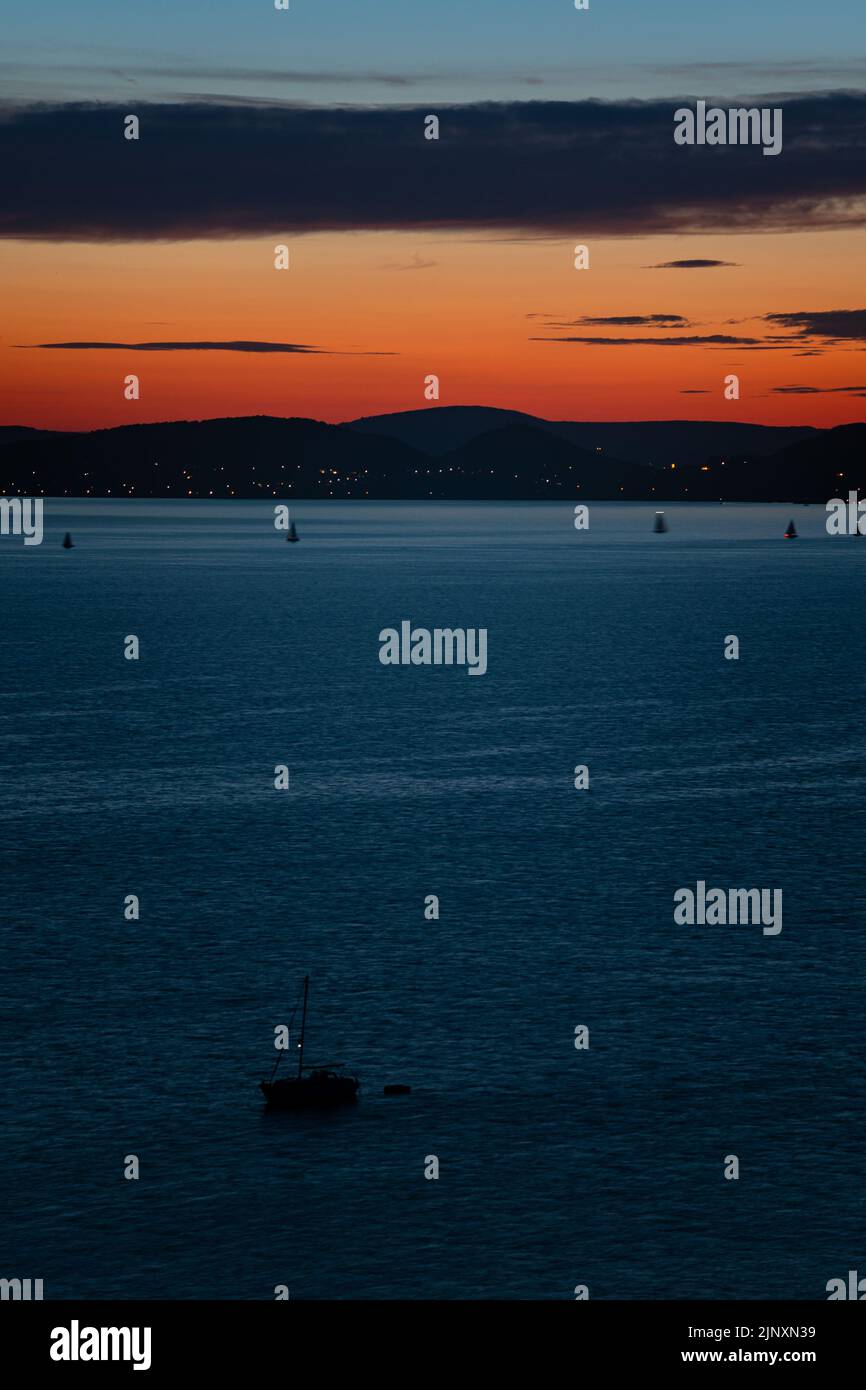 Segelboot auf dem Plattensee kontrastiert mit einem bunten Dämmerungshimmel über den Hügeln auf der anderen Seite des Sees Stockfoto