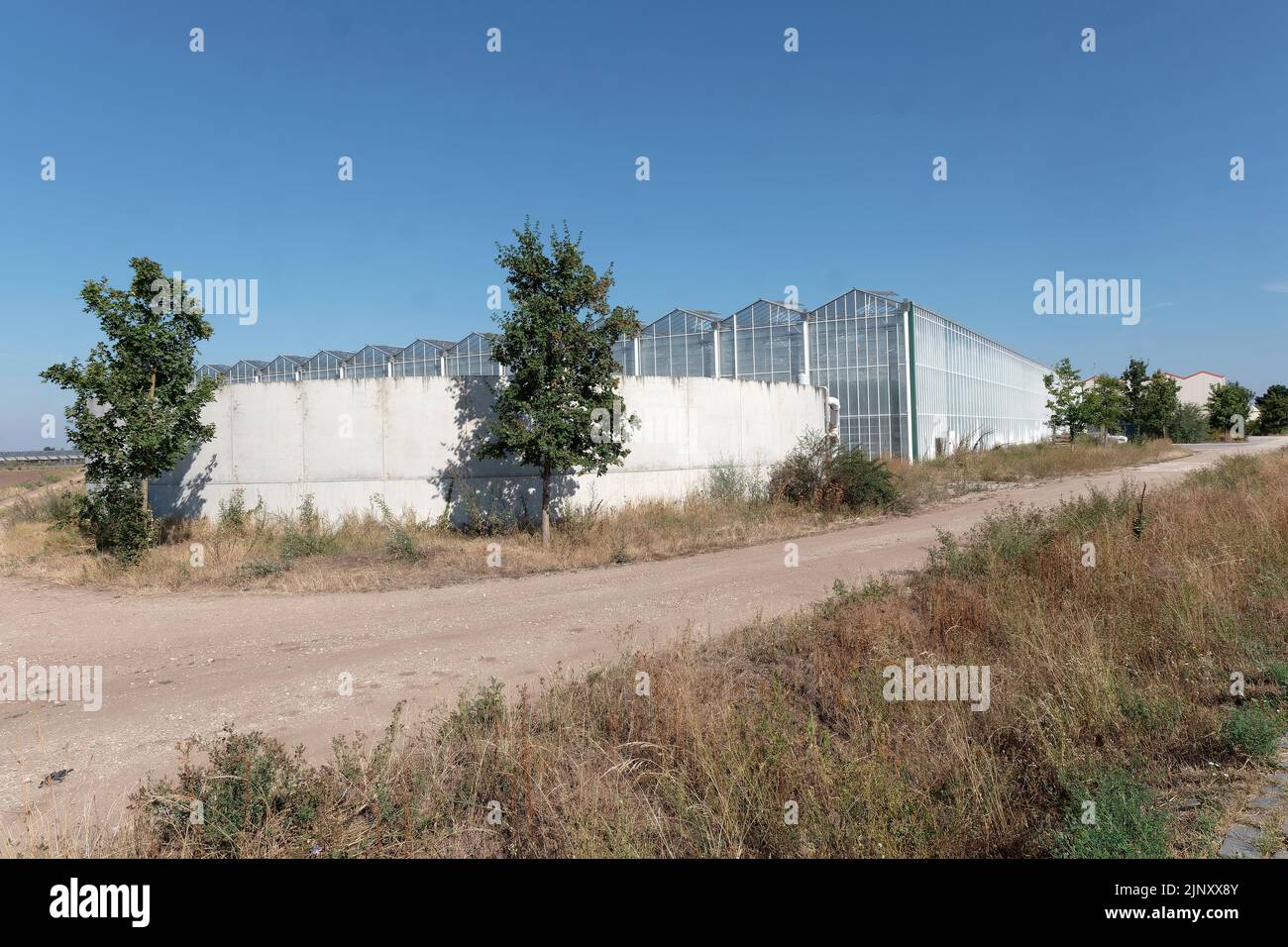 Nahrungsmittelproduktion bei zunehmender Hitze und Trockenheit: Wasserzisterne vor einem großen kommerziellen Glasgewächshaus Stockfoto
