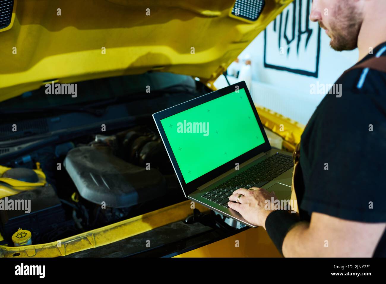 Hände eines jungen Reparaturwerkers oder Technikers, der auf dem Laptop-Tastenfeld tippt, während er vor der offenen Motorhaube des Autos steht und Diagnosen durchführt Stockfoto