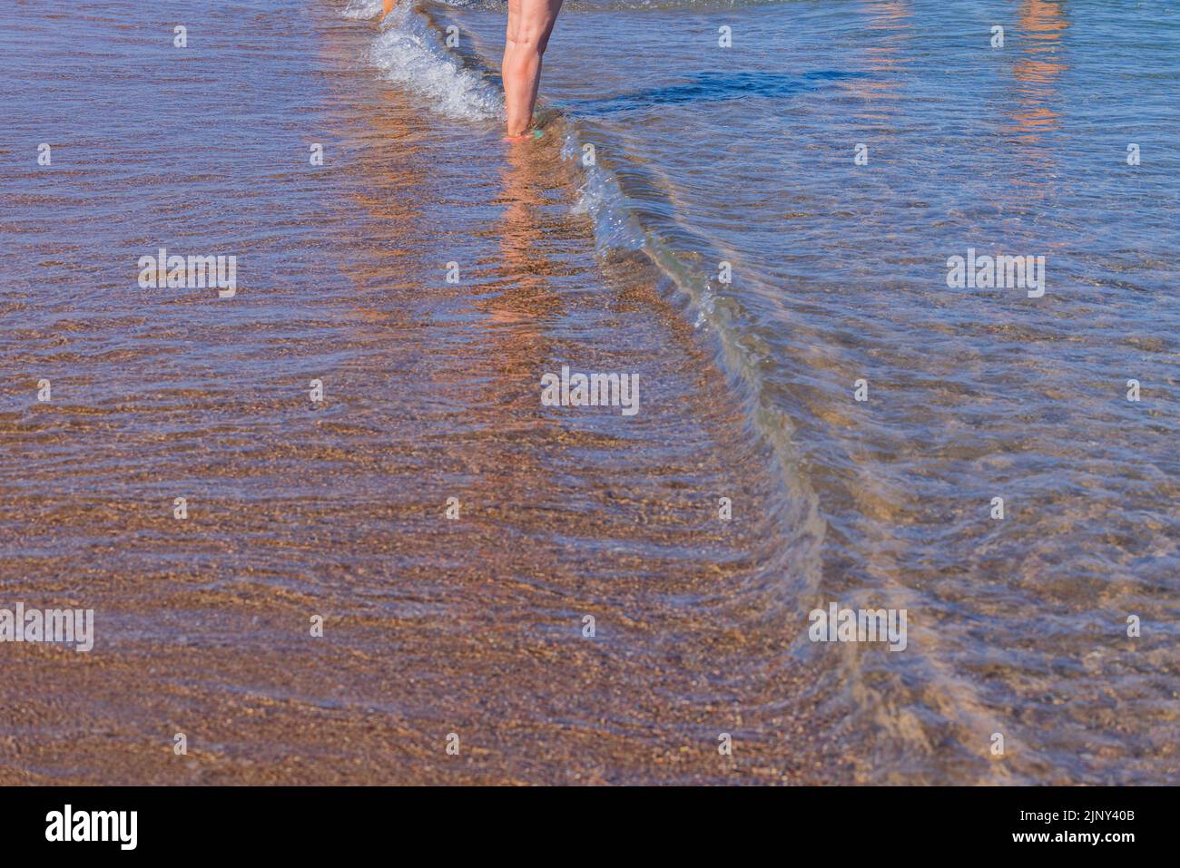 Blick auf die Beine eines Mannes, der vom Ufer des Sandstrandes ins Meer eindringt. Griechenland. Stockfoto