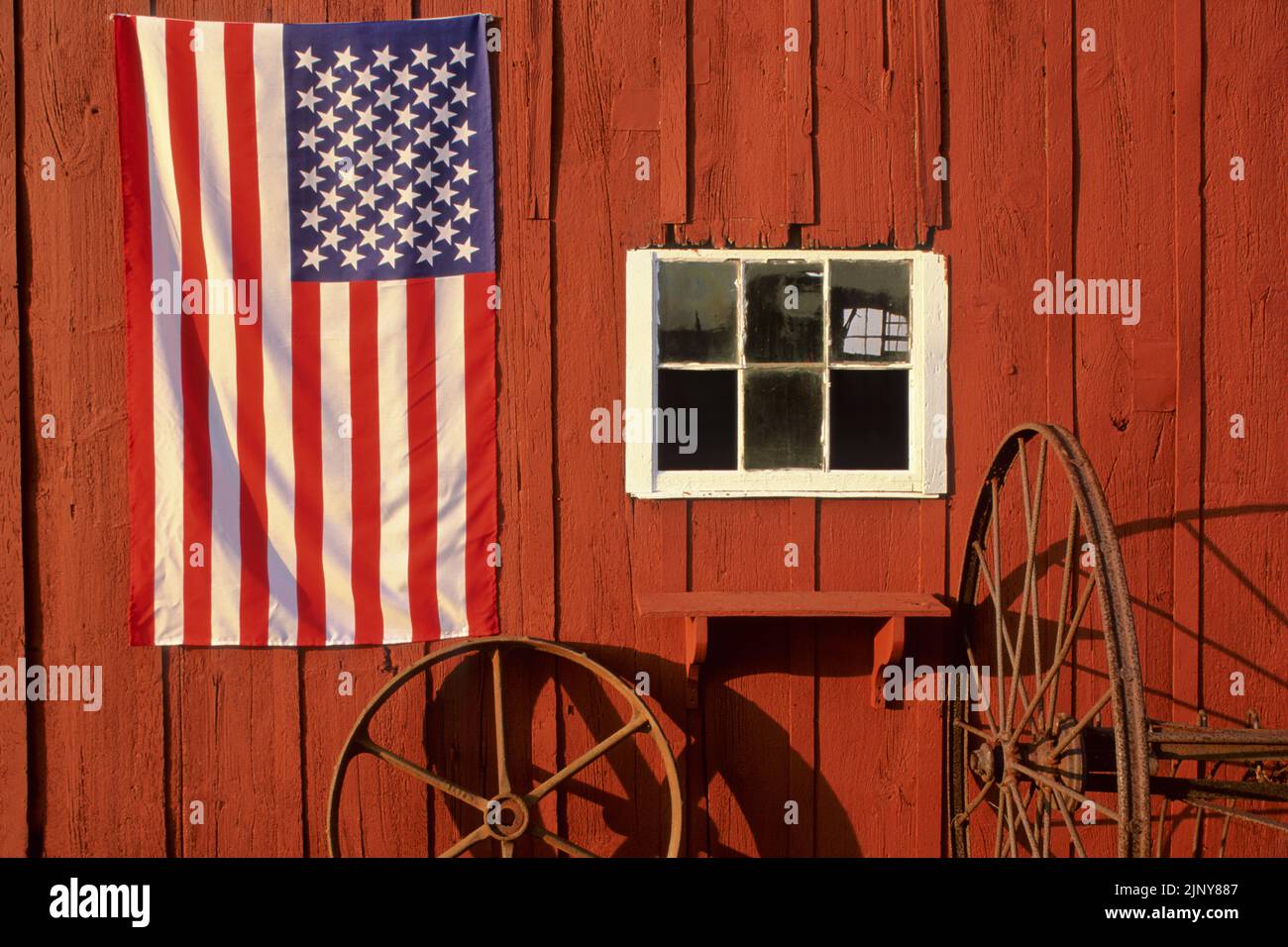 Amerikanische Flagge auf einer alten roten Scheune mit einem Fenster, Heurechen und Rad, Monroe, New Jersey, USA US NJ USA Vintage Farming close up Stockfoto