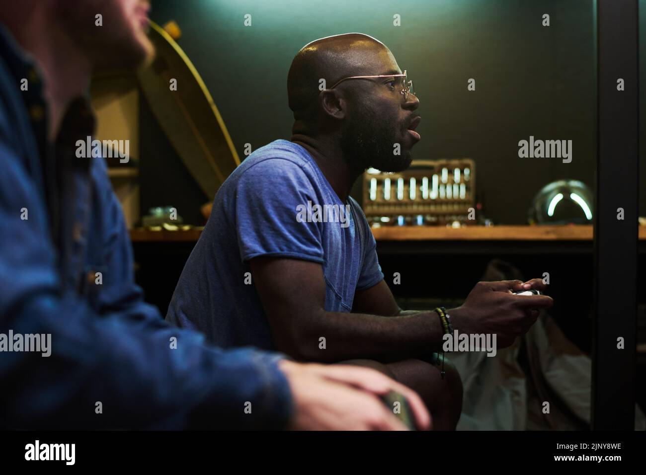 Junger, enthusiastischer schwarzer Mann mit Gamepad, der während des Videospiels auf der Couch vor dem fernsehbildschirm sitzt und Tasten auf dem Joystick drückt Stockfoto