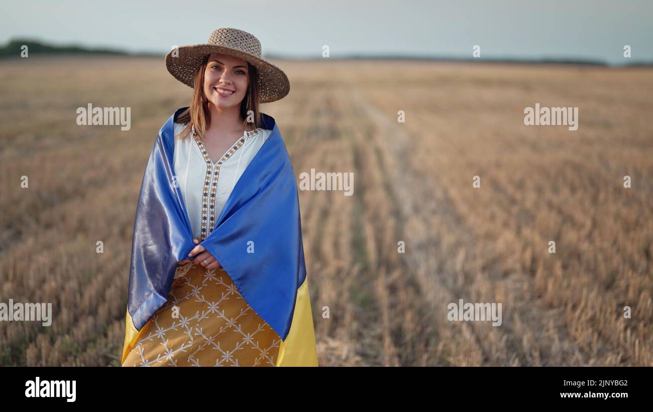 Lächelnde ukrainische Frau mit Nationalflagge im Weizenfeld nach der Ernte. Charmante ländliche Dame in Stickerei vyschywanka. Ukraine, Unabhängigkeit Stockfoto