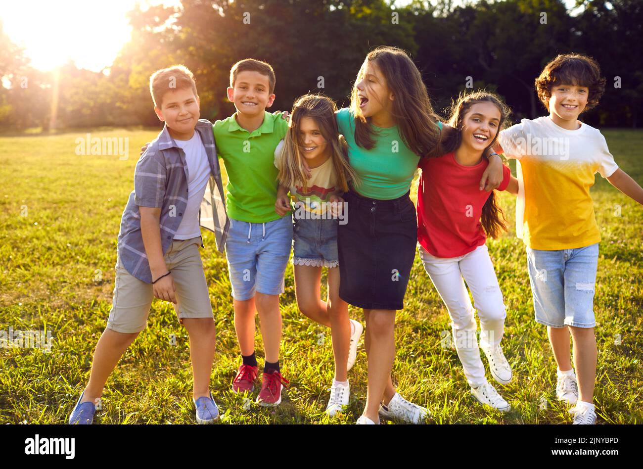 Eine Gruppe fröhlicher Kinder, die im grünen Park spazieren und sich umarmen Stockfoto