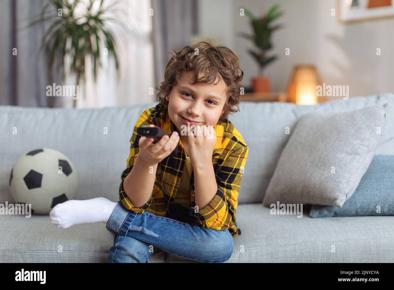 Super Fernseher für Kinder. Lustiger kleiner Junge, der Videos oder Filme mit Fernbedienung auswählt, zu Hause auf dem Sofa sitzt, Fernseher pov Stockfoto