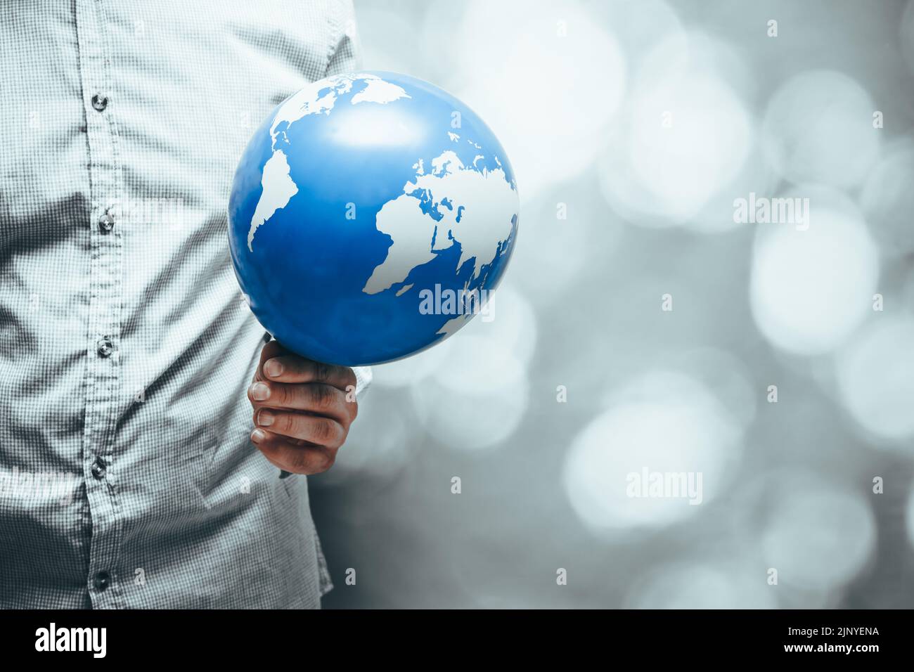 Ein Mann hält einen erdförmigen Ballon in seiner rot-heißen Hand, künstlerische Farben, kreatives ökologisches Konzept, Globale Erwärmung, menschlicher Einfluss auf den Planeten, Stockfoto