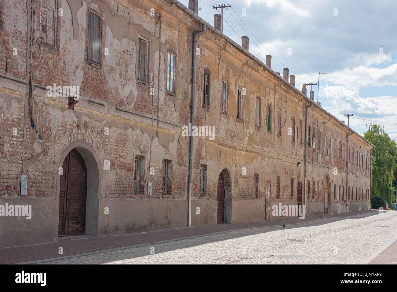 Fenster säumen die Außenwand eines abgenutzten Backstein- und Gipszitadellengebäudes in Ossjek, Kroatien. Das lange Gebäude ist in Verfall. Stockfoto