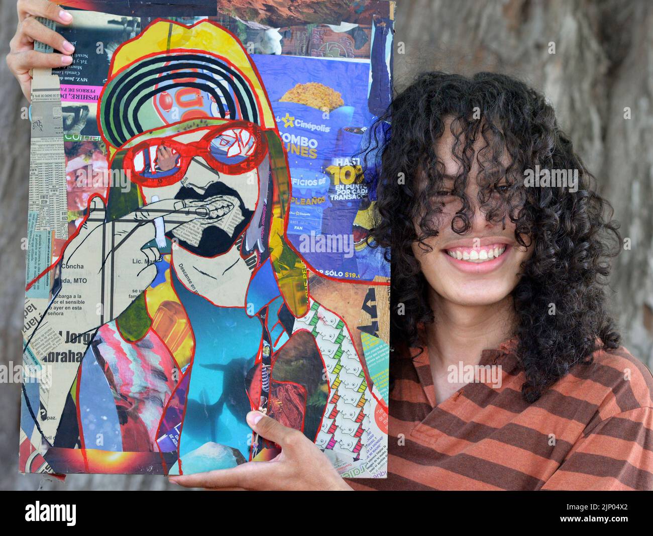 Lächelnd schöner junger mexikanischer Künstler mit langen schwarzen Lockenhaaren zeigt ein gemischtes Collage-Porträt von Kurt Cobain. Stockfoto