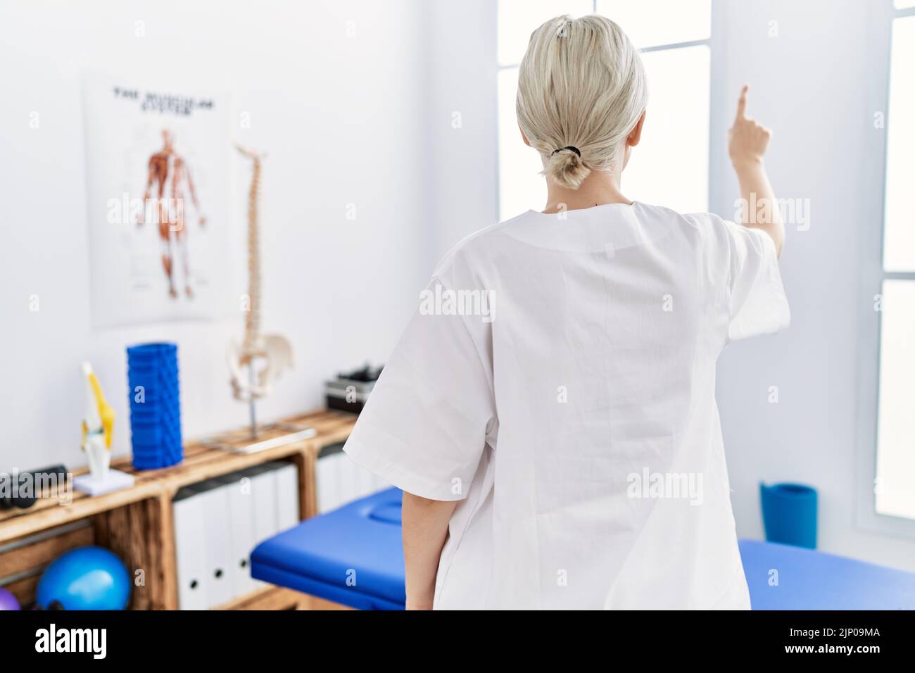 Junge kaukasische Frau, die in der Schmerzklinik arbeitet, posiert rückwärts und zeigt mit der Fingerhand nach vorne Stockfoto