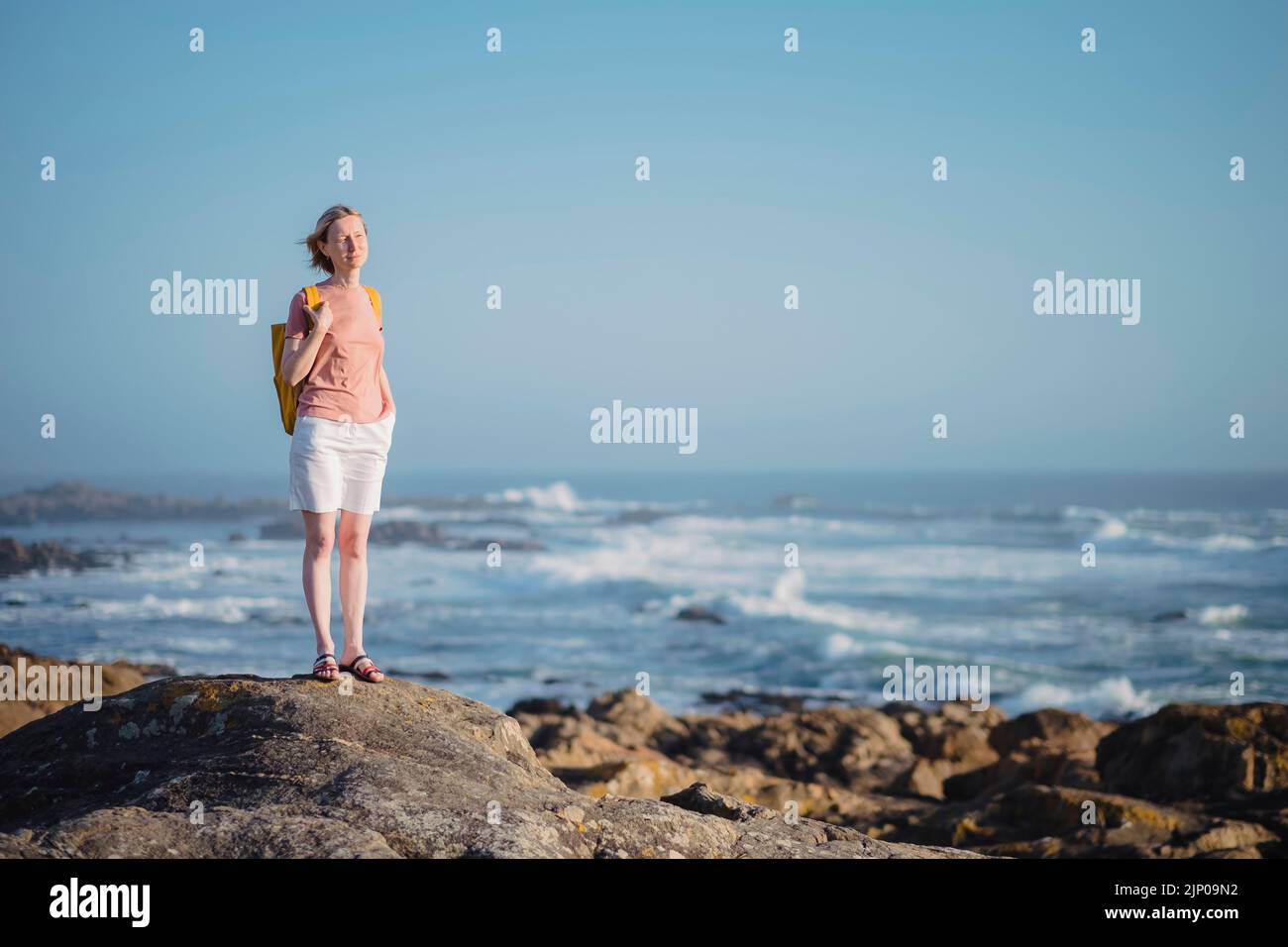 Eine Frau mit Rucksack steht auf den Felsen in der Nähe des Meeres. Stockfoto