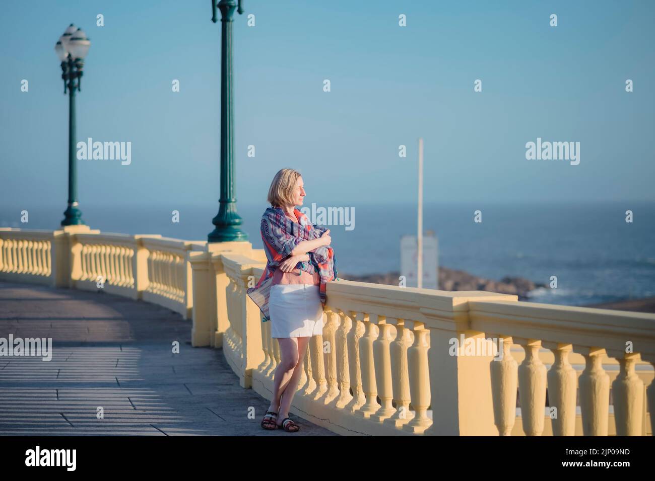 Eine Frau mit Rucksack steht auf der Promenade am Meer. Stockfoto