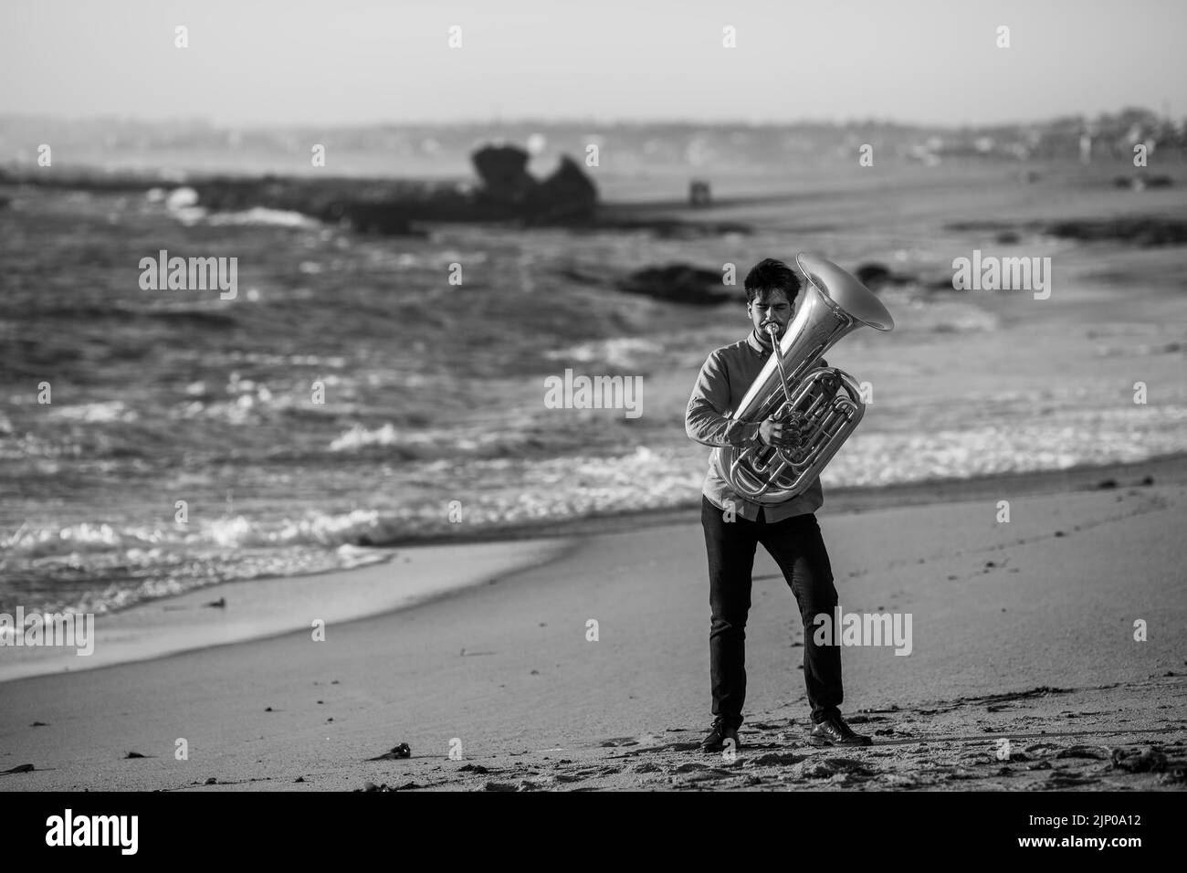 Ein Musiker, der am Atlantikstrand eine Tuba spielt. Schwarzweiß-Foto. Stockfoto