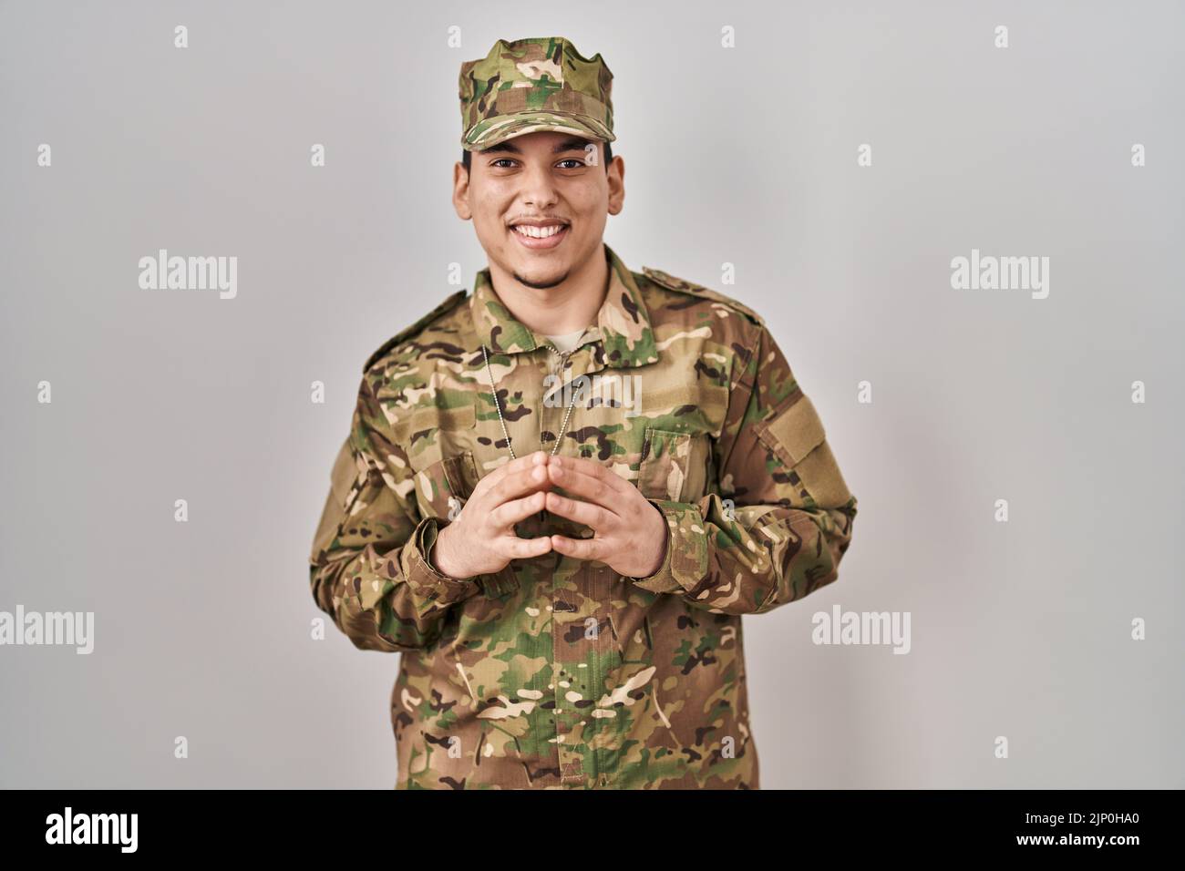 Junger arabischer Mann trägt Tarnuniform der Armee Hände zusammen und die Daumen kreuzten lächelnd entspannt und fröhlich. Erfolg und optimistisch Stockfoto