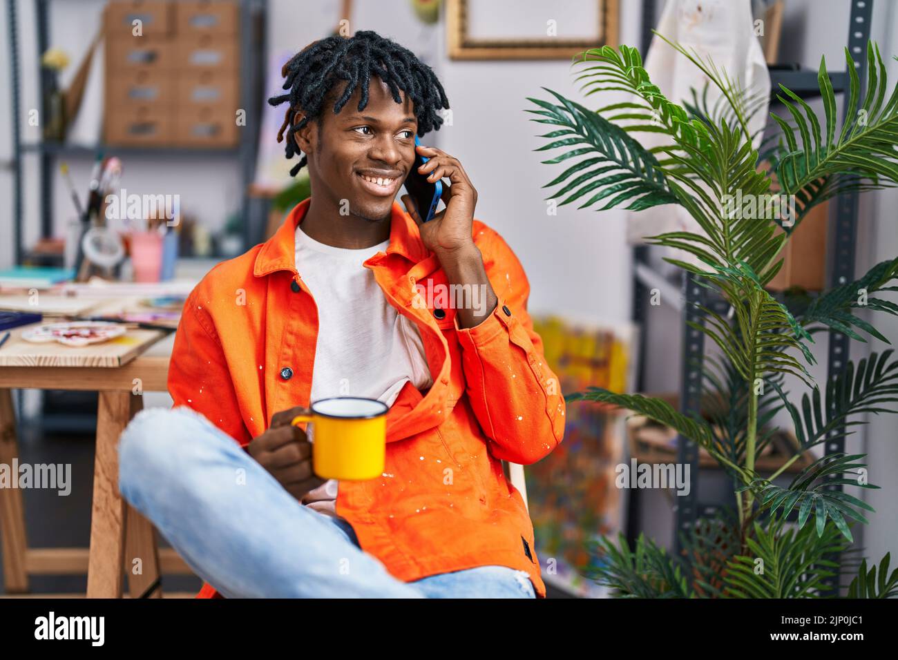afroamerikanischer Künstler trinkt Kaffee-Talkking auf dem Smartphone im Kunststudio Stockfoto