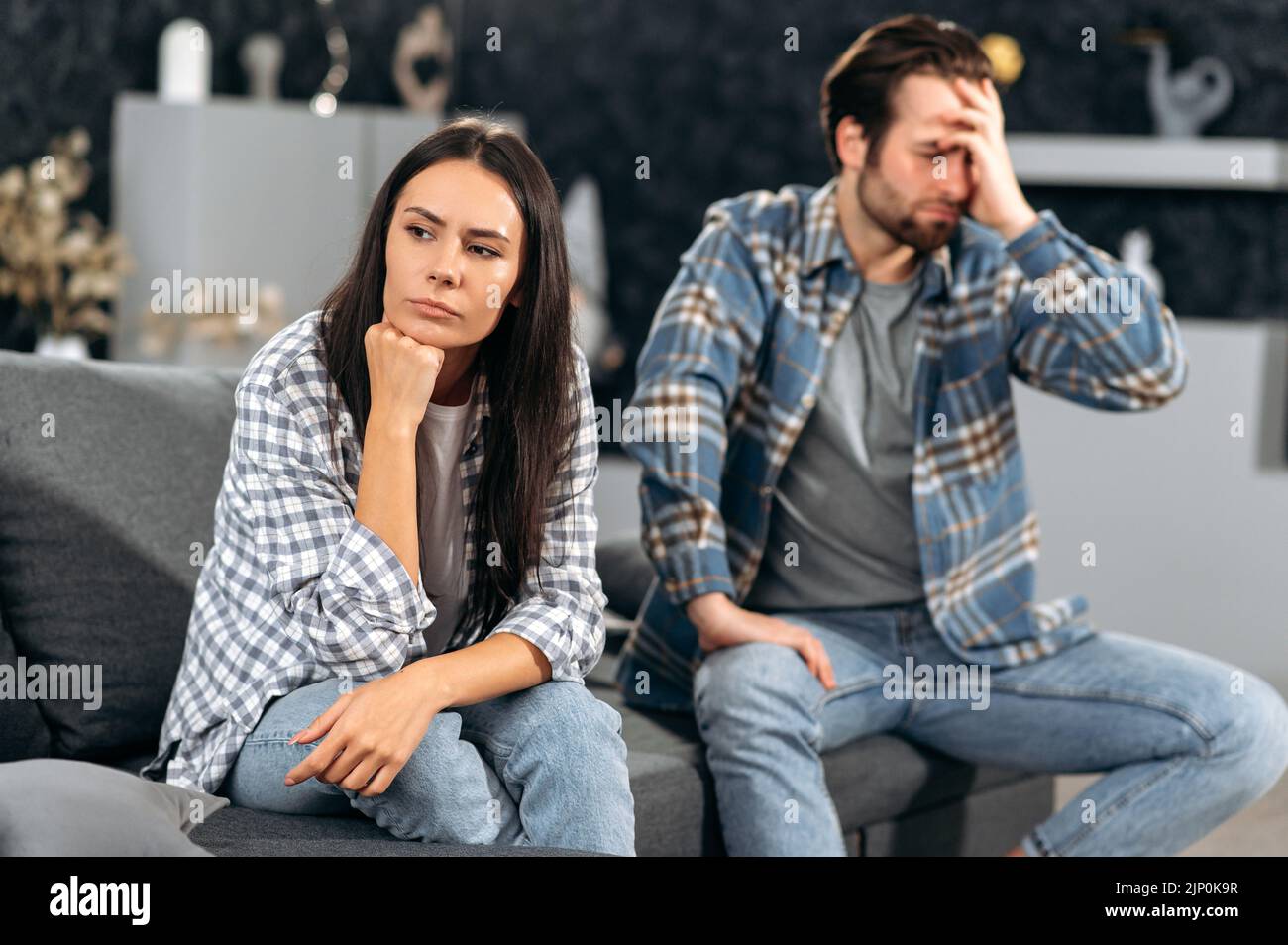 Ein Streit in der Beziehung eines kaukasischen Paares, die Ehepartner zanken über Meinungsverschiedenheiten, sie sitzen auf einem Sofa im Wohnzimmer, sie werden gegenseitig beleidigt, sie schauen in verschiedene Richtungen Stockfoto