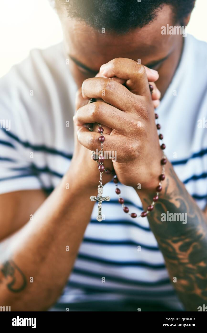 Er hört all eure Gebete. Ein junger Mann hält während des Gebets seinen Rosenkranz. Stockfoto