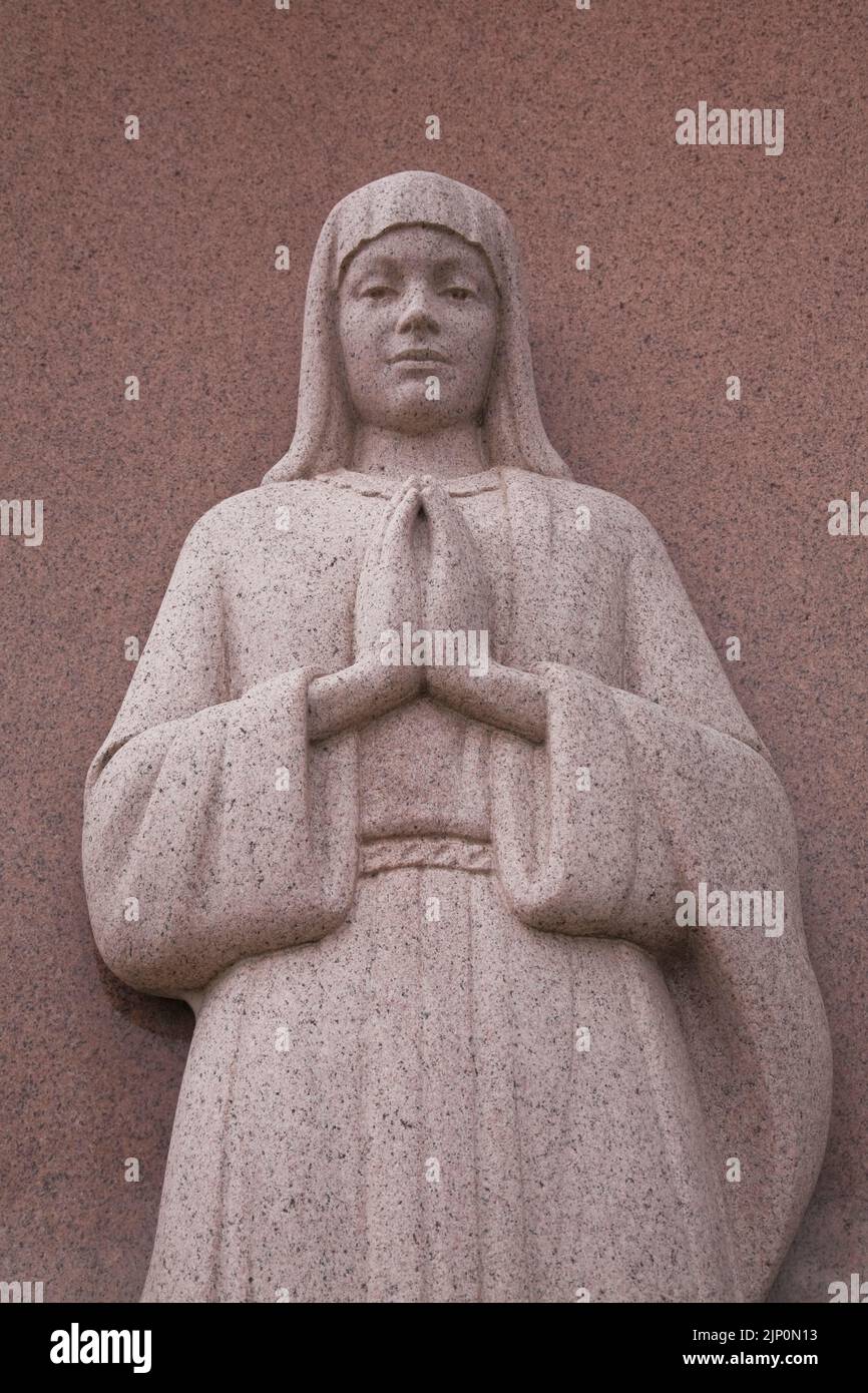 Religiöse, braune Granit-Statue einer Nonne, die auf einem Denkmal auf einem Friedhof betet. Stockfoto