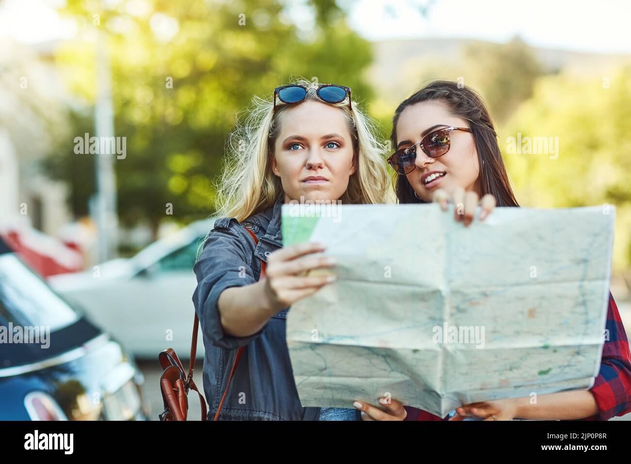 Sich zu verlaufen ist Teil der Reise. Zwei schöne Freundinnen, die auf einer Karte nach Wegbeschreibungen in der Stadt suchen. Stockfoto