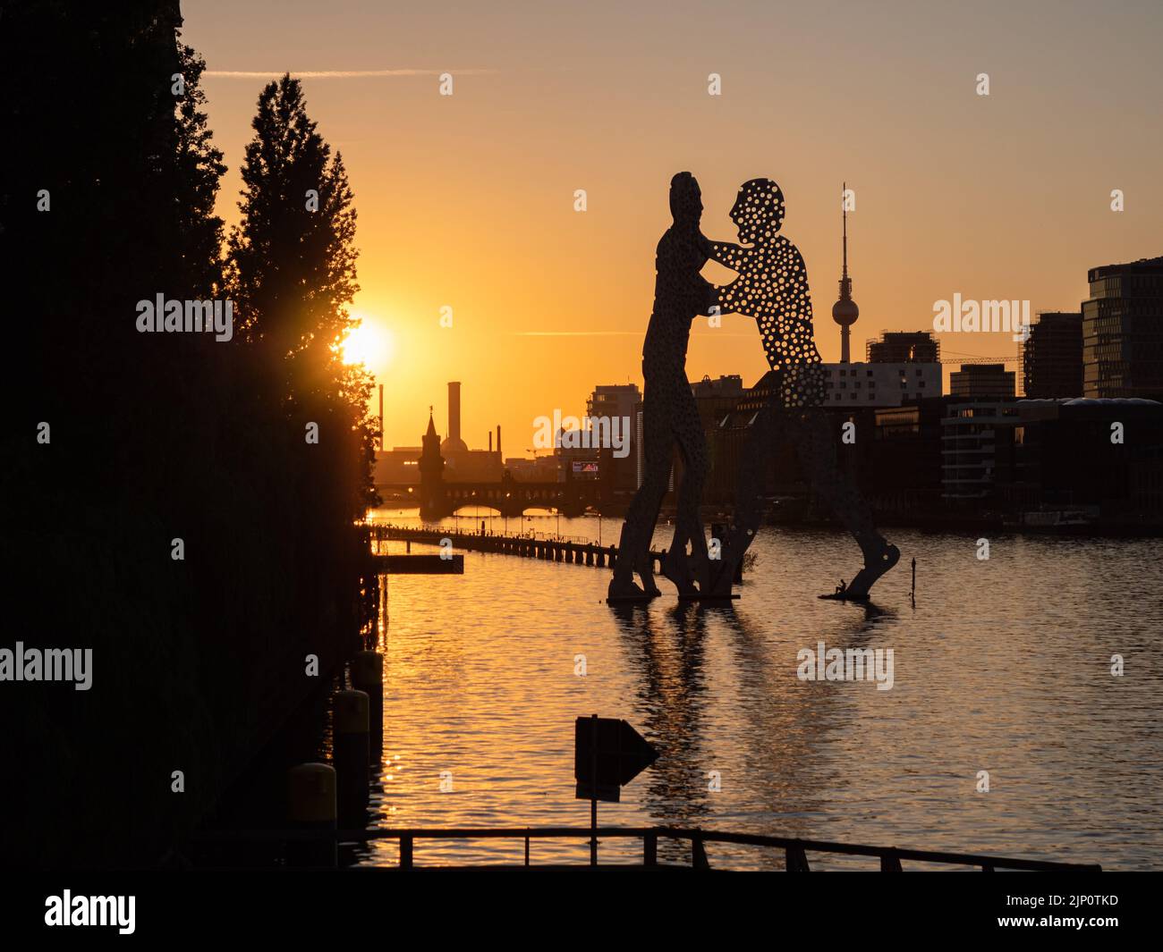 Sonnenuntergang auf der Spree in Berlin. Die Skulptur Molecule man von Jonathan Borofsky befindet sich vor der Skyline der Stadt mit dem Fernsehturm. Stockfoto