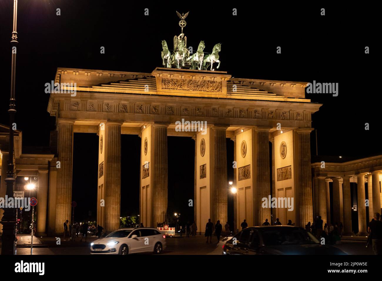 Das Brandenburger Tor ist bei Nacht beleuchtet. Dieses Gebäude ist ein Wahrzeichen Berlins und ein berühmtes Reiseziel. Die Menschen sind am Pariser Platz. Stockfoto