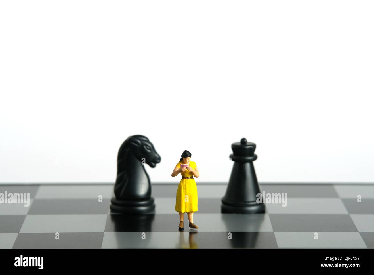 Miniatur Menschen Spielzeug Figur Fotografie. Defensives oder Angriffsstrategien-Konzept. Eine Schülerin, die zwischen Pferd und Schloss Schachbrett Bauer k steht Stockfoto