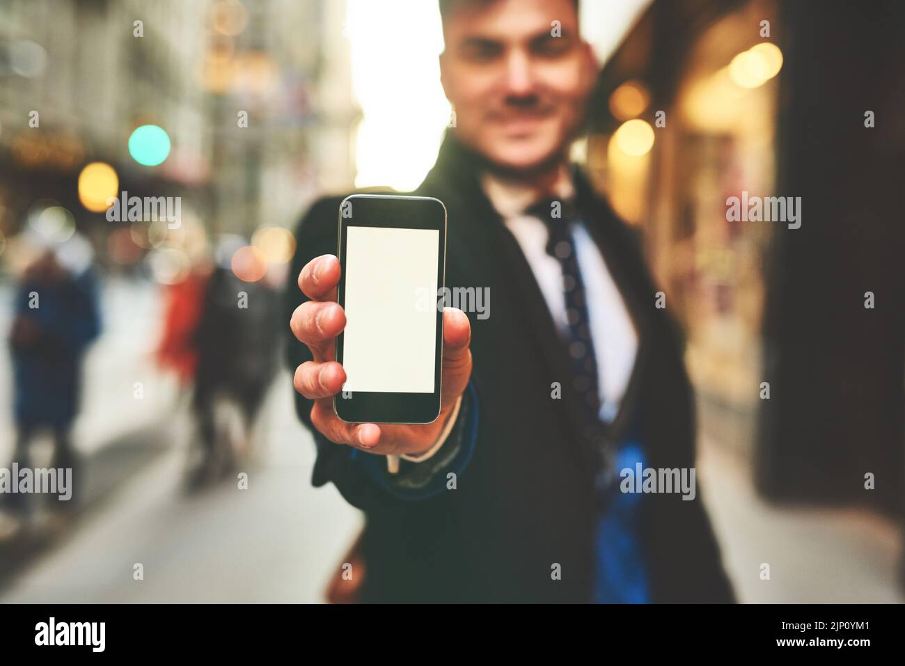 Was halten Sie von diesem Foto? Nahaufnahme eines fröhlichen jungen Mannes, der ein Handy hochhält und der Kamera den Bildschirm draußen in der Stadt zeigt Stockfoto