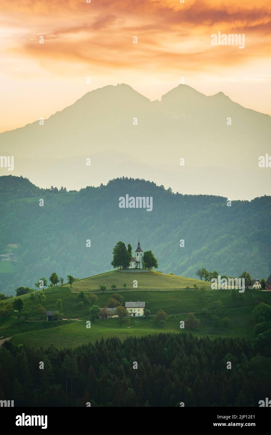 Sveti Tomaz Kirche, Slowenien - Luftbild Bergkirche St. Thomas, schöner goldener Sonnenaufgang über den Kamnik-Savinja Alpen, Skofja Loka. Stockfoto