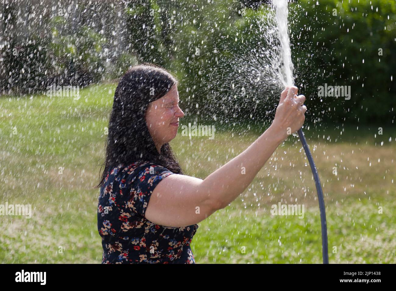 Umea, Norrland Schweden - 1. Juli 2022: Frau sprüht in der Hitzewelle Wasser auf sich selbst mit einem Wasserschlauch Stockfoto