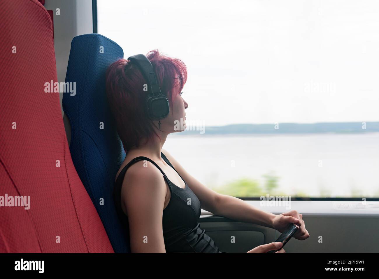 Die junge Frau fährt im Zug, hört Musik und schaut aus dem Fenster Stockfoto