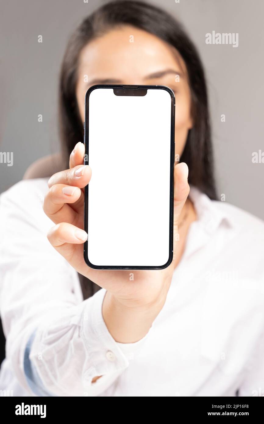 Die junge Frau hält das Smartphone mit dem Smartphone vor ihrem Gesicht. Empfehlungskonzept. Neues Mobiltelefon mit weißem leeren Bildschirm für Mockup. Stockfoto