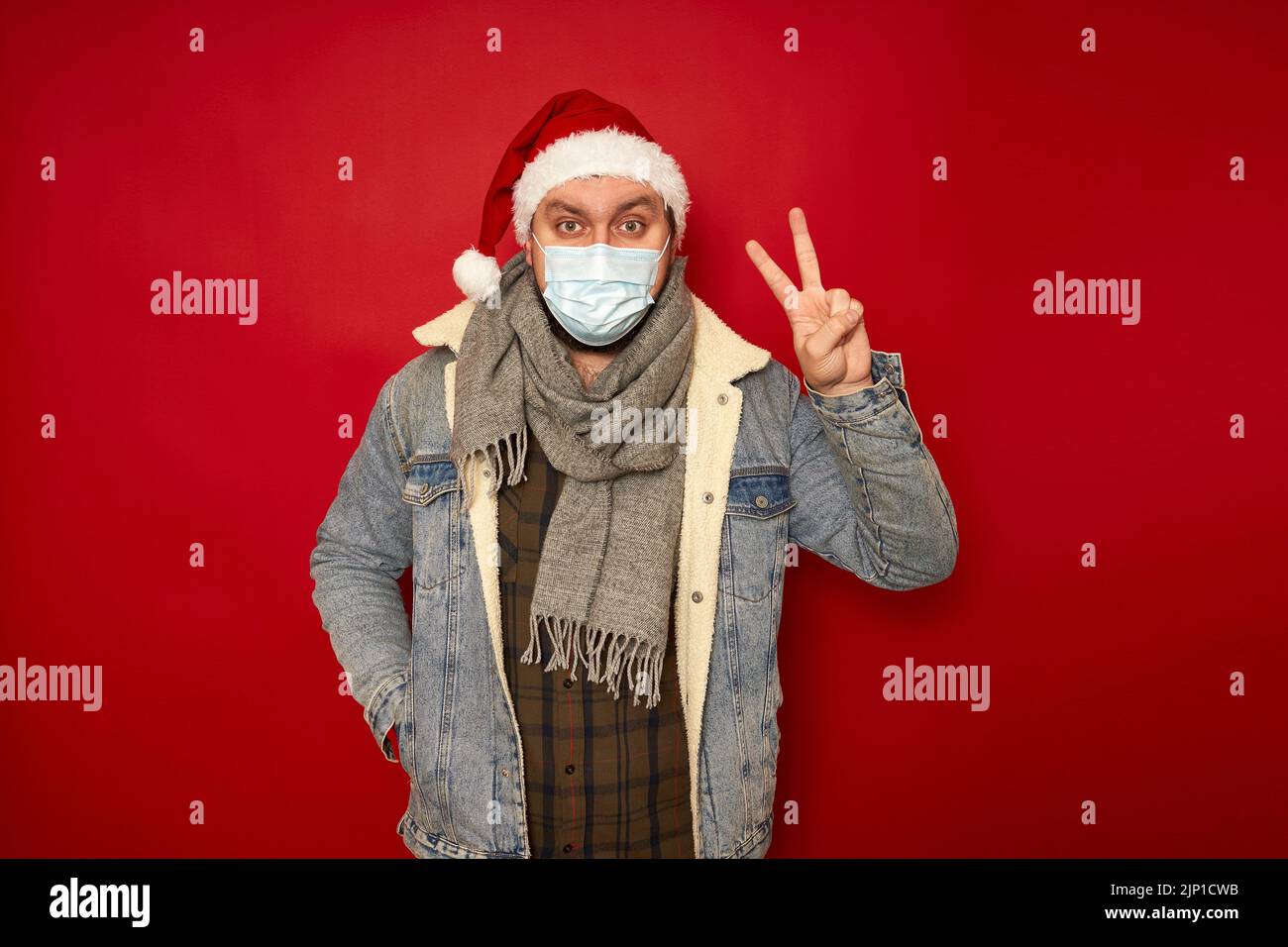 Mann in Weihnachtshut, medizinische Maske auf Gesicht zeigt Frieden Sieg Zeichen Hand isoliert Studio Hintergrund Stockfoto