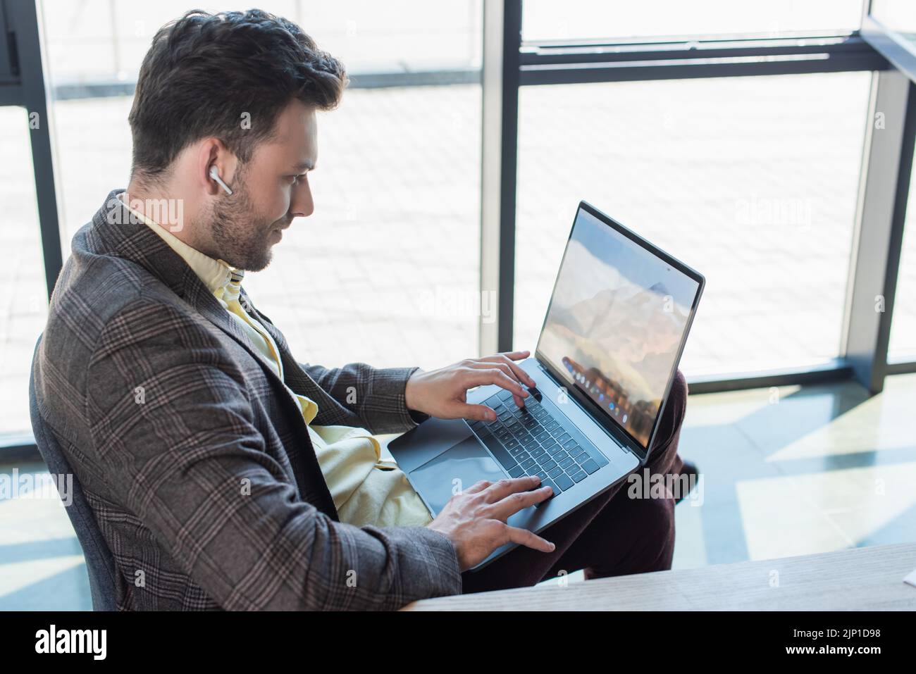 Seitenansicht eines Geschäftsmanns im Kopfhörer, der im Büro einen Laptop benutzt, Stockbild Stockfoto