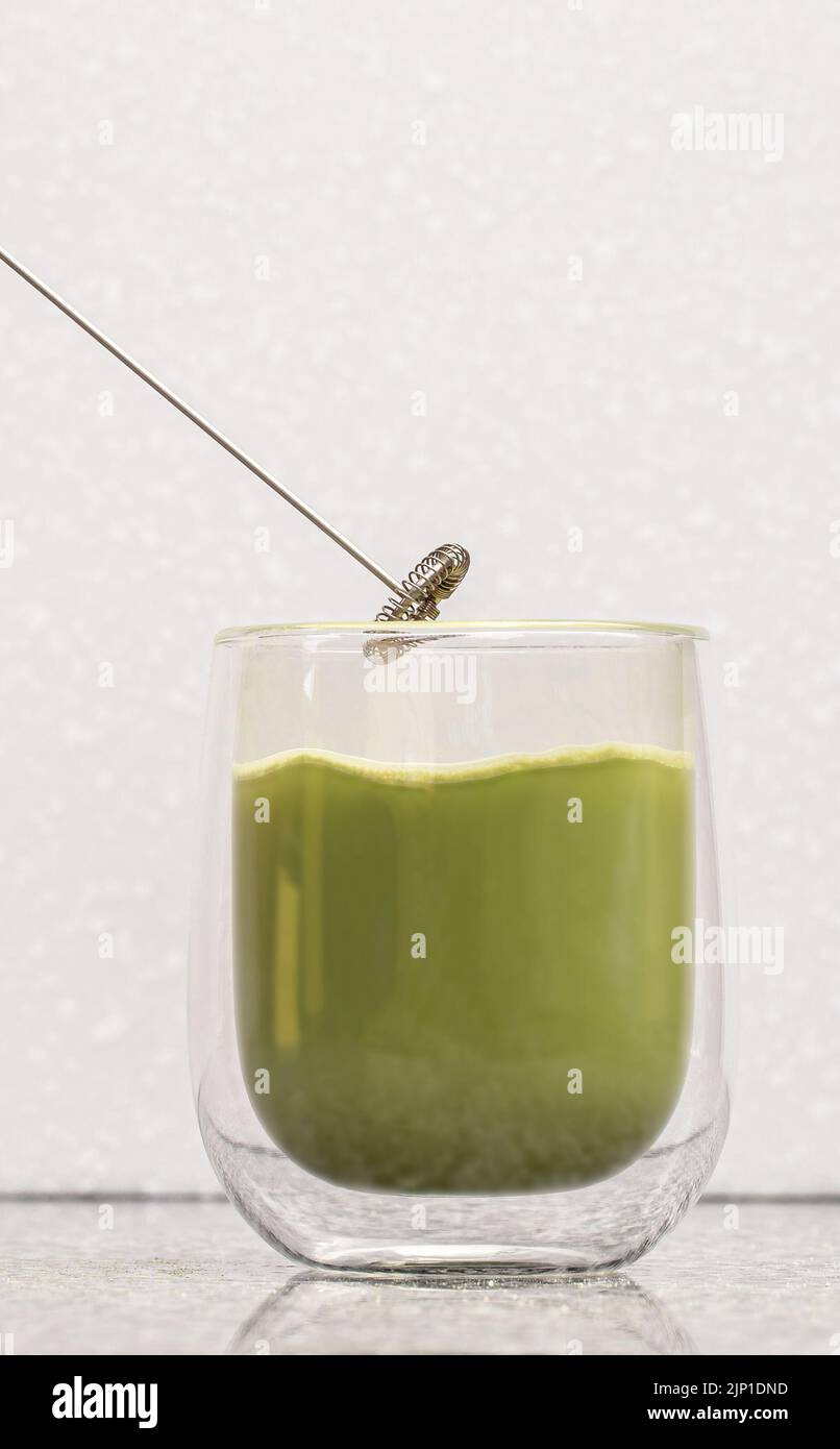 Grüner Matcha-Latte-Tee in einem Glas. Grüner Matcha Latte wird in ein transparentes Glas mit doppeltem Boden gegossen Stockfoto