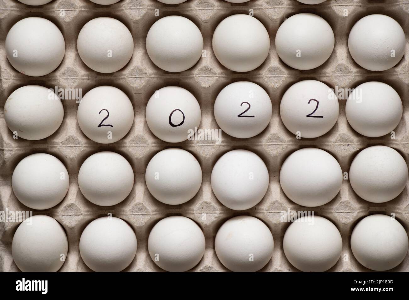 2022 steht auf weißen Hühnereiern in einem Papiertablett, das Jahr 2022 steht auf Eiern Stockfoto