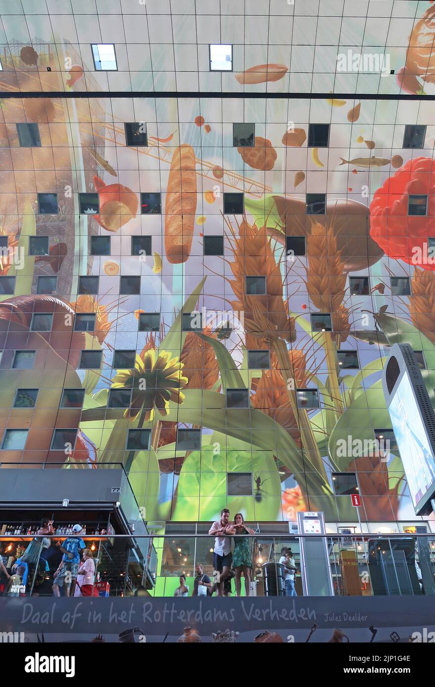 Die Innenansicht der Markthall (Markthalle) in Rotterdam zeigt die geschwungene Decke mit einem riesigen Wandgemälde mit Obst und Gemüse. Paar im Vordergrund. Stockfoto