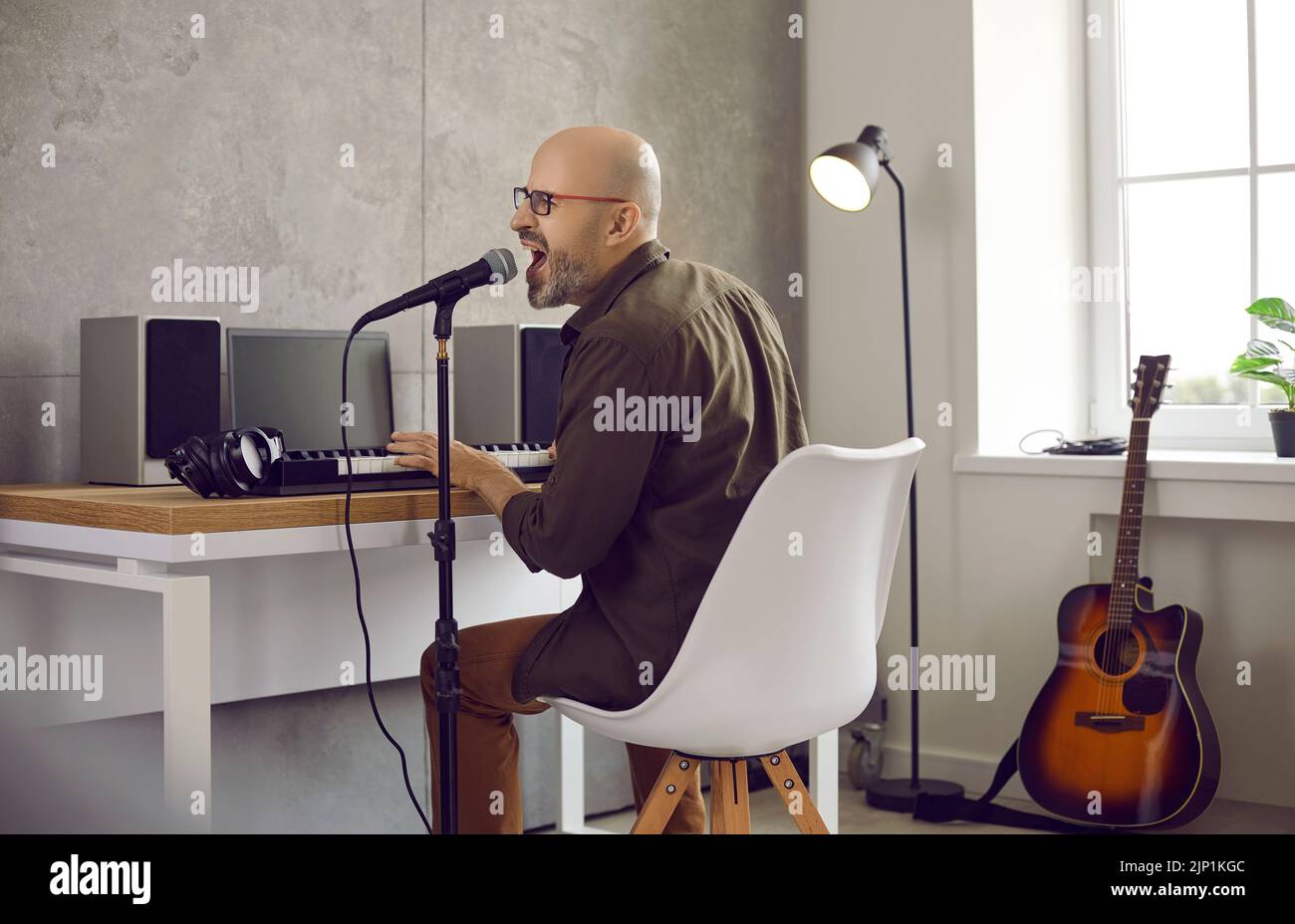 Kreativer Musiker, der in seinem Studio auf elektronischem Keyboard singt und Musik spielt Stockfoto