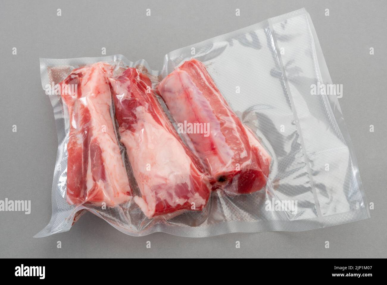 Schweineribs in vakuumverpackter Verpackung, versiegelt für das Sous-Vide-Kochen auf grauem Hintergrund in der Draufsicht. Stockfoto