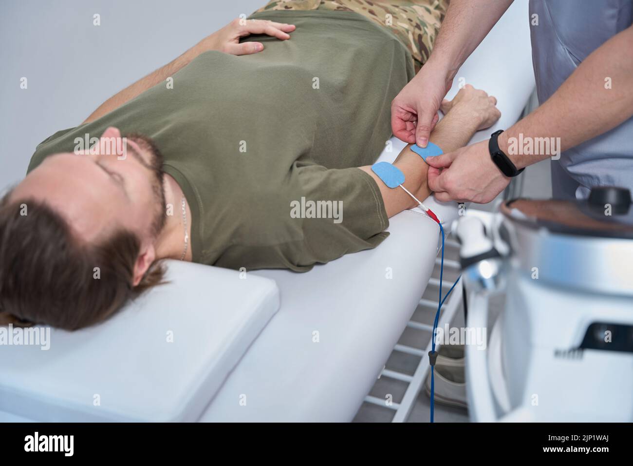 Der Physiotherapeut befestigt die Elektroden am Patientenarm Stockfoto