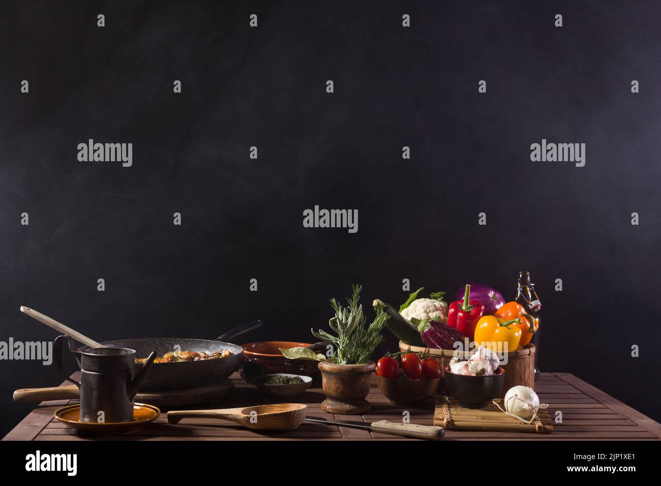 Frisches Gemüse, das in einer Pfanne gekocht wird, die noch auf dem Holztisch einer Restaurantküche dampft. Platz oben kopieren Stockfoto