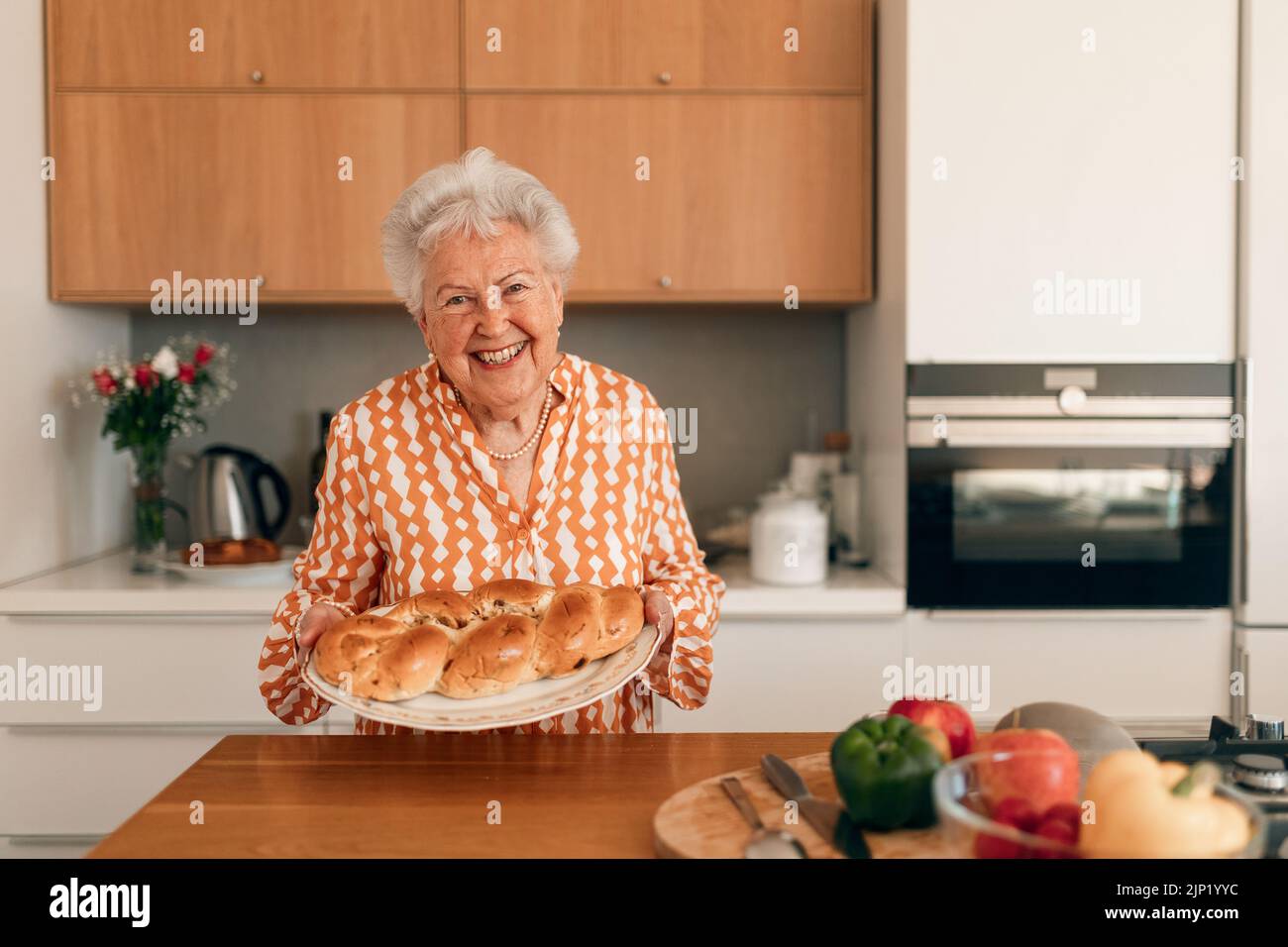 Glückliche ältere Frau mit hausgemachtem süßen geflochtenen Brot mit Rosinen. Stockfoto