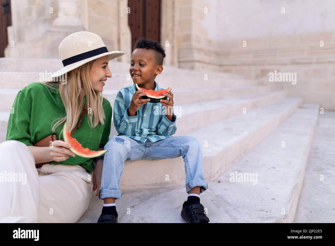 Multirassischer Sohn mit Mutter, der an heißen sonnigen Tagen Wassermelone auf der Straße isst, Reisekonzept für Sommerferien. Stockfoto