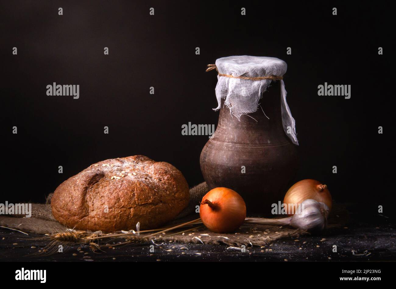 Stillleben Steingutkrug mit Milch auf dem Tisch mit Vorrat, Brot, Zwiebeln und Schnittlauch Stockfoto