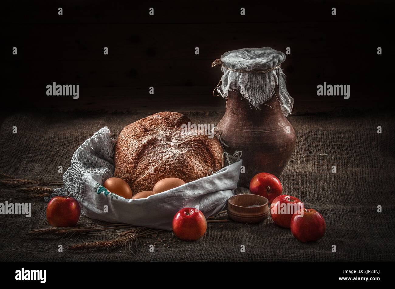 Stillleben Steingutkrug mit Milch auf dem Tisch mit Vorrat, Brot, Eiern und Äpfeln, bäuerliche Nahrung Stockfoto