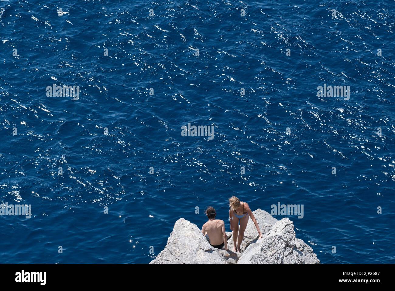 Junges Paar, das im Sommer in Hydra Griechenland von Felsen ins Meer springen wird Stockfoto