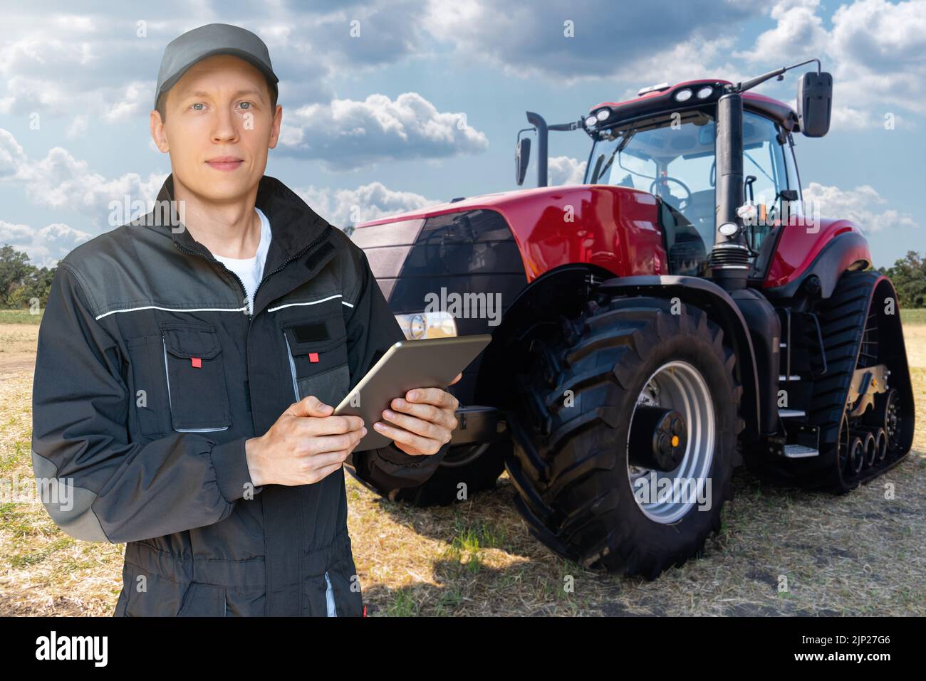 Landwirt mit einem digitalen Tablet auf dem Hintergrund eines landwirtschaftlichen Traktors Stockfoto