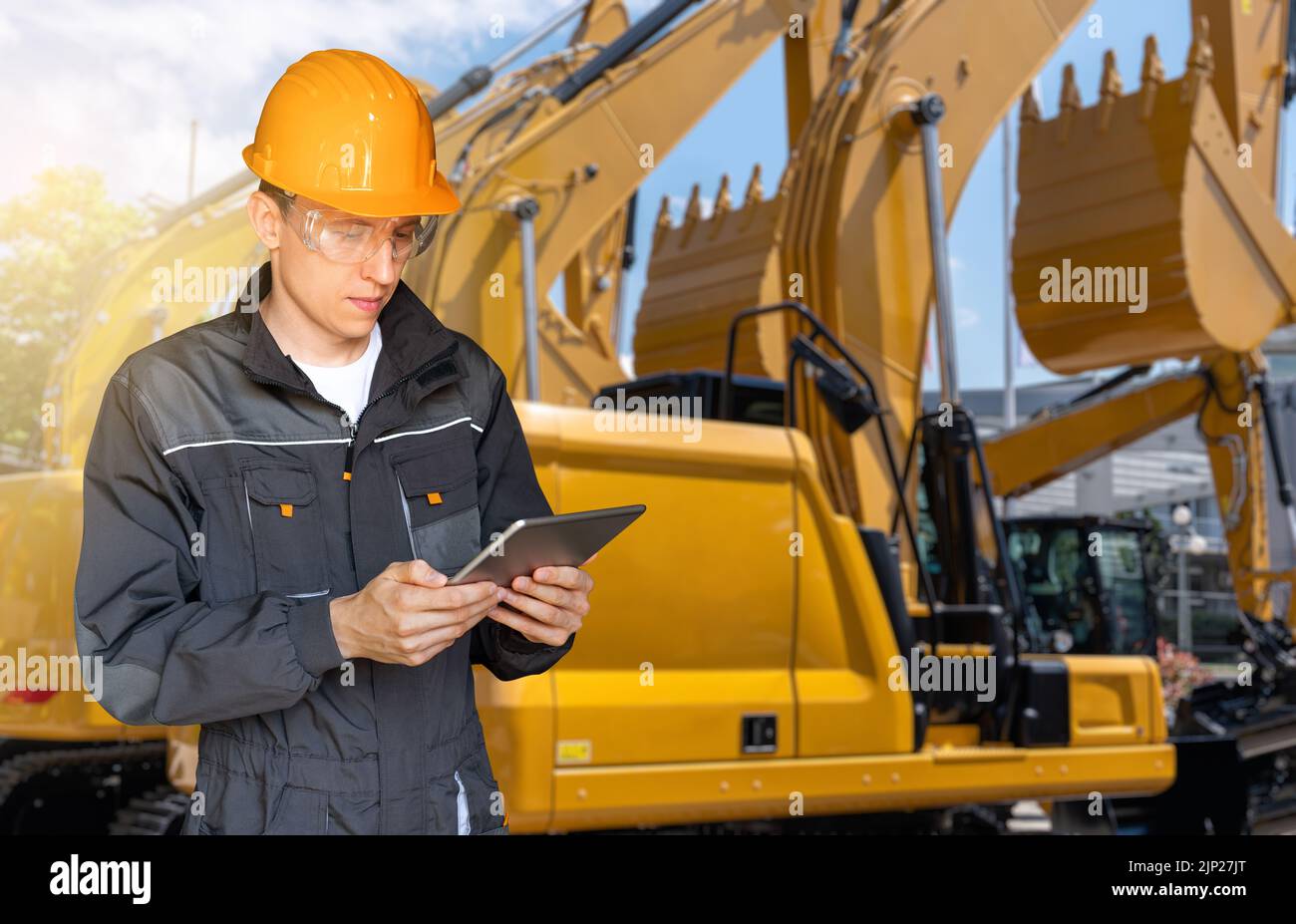 Ingenieur in einem Helm mit einem digitalen Tablet auf dem Hintergrund von Baumaschinen Stockfoto