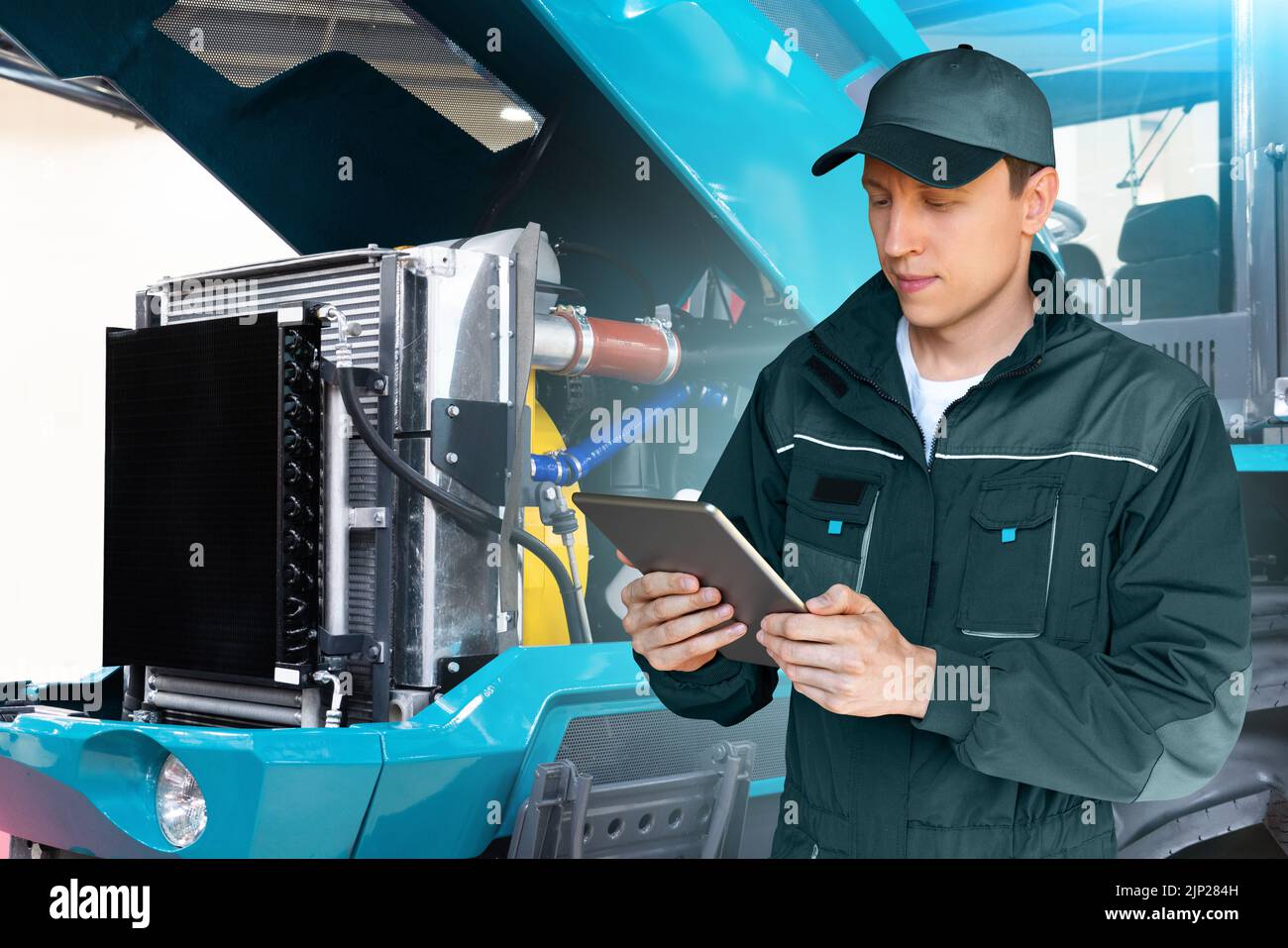 Servicearbeiter mit digitalem Tablet auf dem Hintergrund des Traktors mit offener Motorhaube Stockfoto