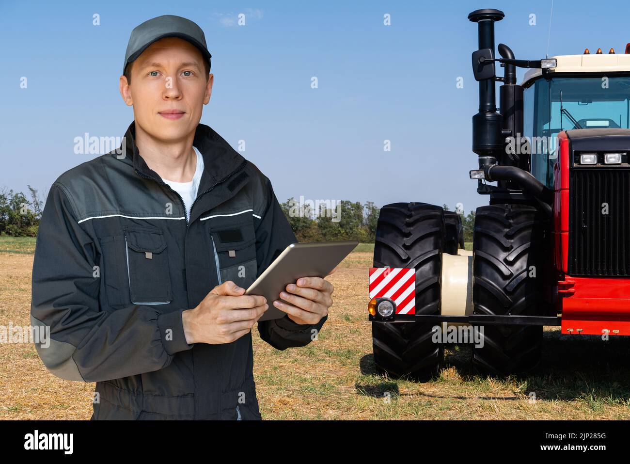 Landwirt mit einem digitalen Tablet auf dem Hintergrund eines landwirtschaftlichen Traktors Stockfoto